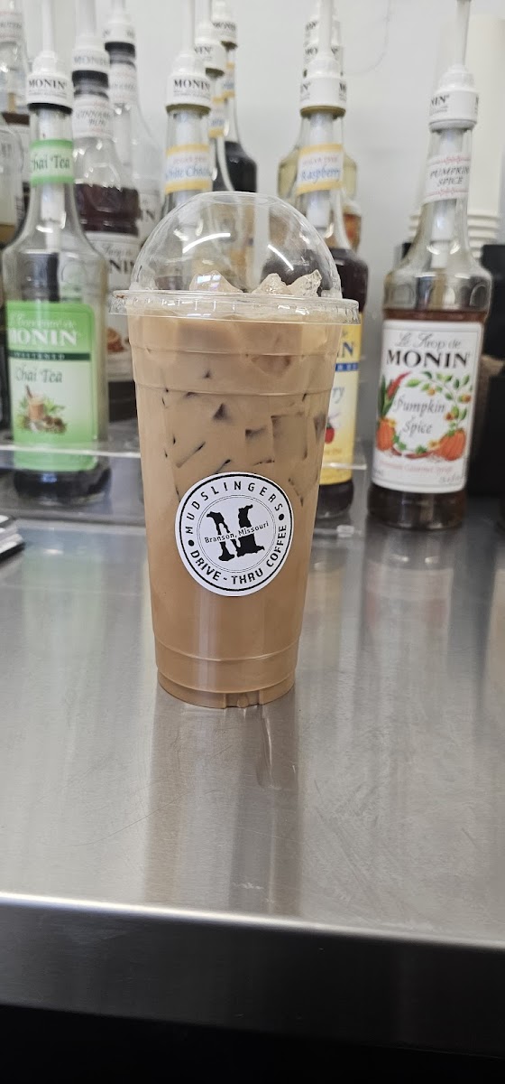 Iced coffee with Mudslingers logo and syrup bottles in the background.
