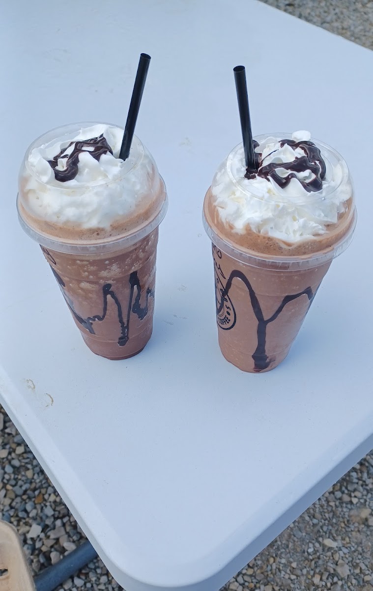 Two frappuccinos with whipped cream and chocolate drizzle.